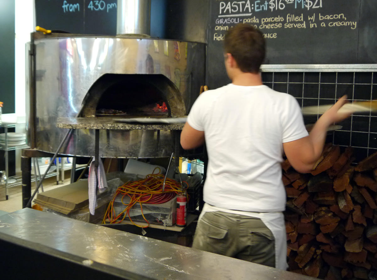 Pizza cook at work - placing pizza in the wood fired oven