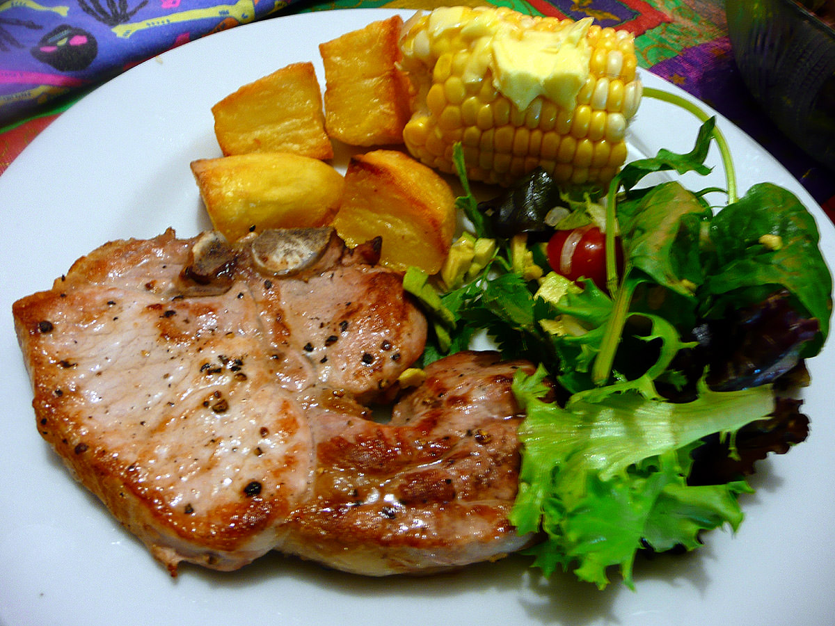 Pork chop, baked potatoes, salad and buttered corn