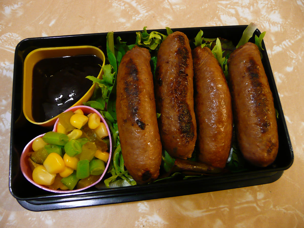 Sausages on a bed of mixed greens, smokey barbecue sauce, and corn kernel, green beans and dill pickle medley