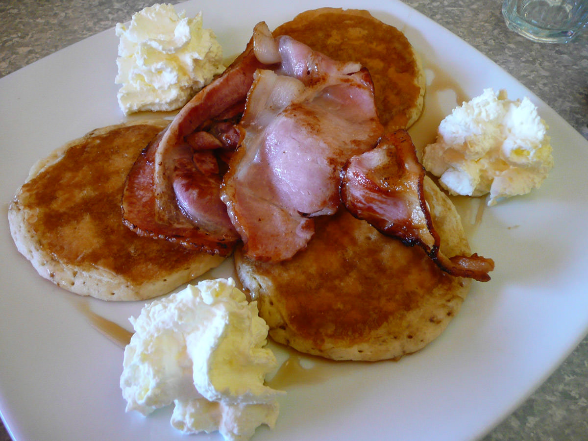 Pancakes with maple syrup and cream and a side of bacon