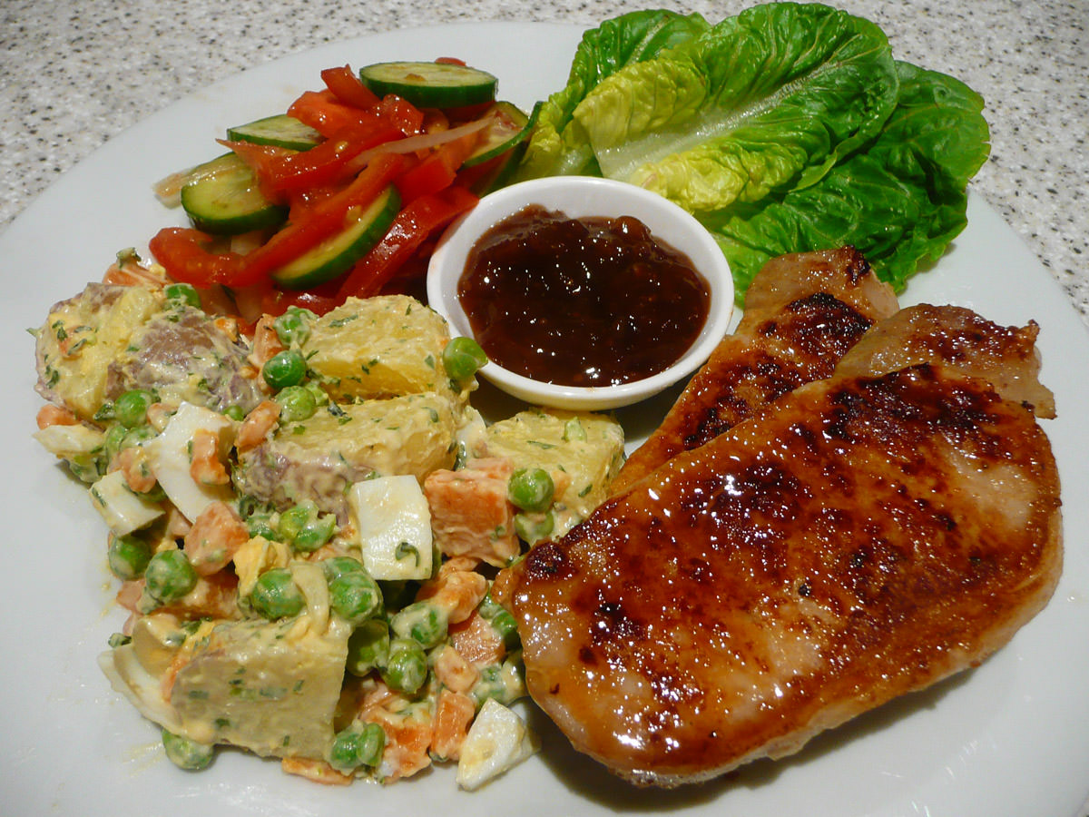 Pork steaks with potato salad, tomato salad and a dish of fruit chutney