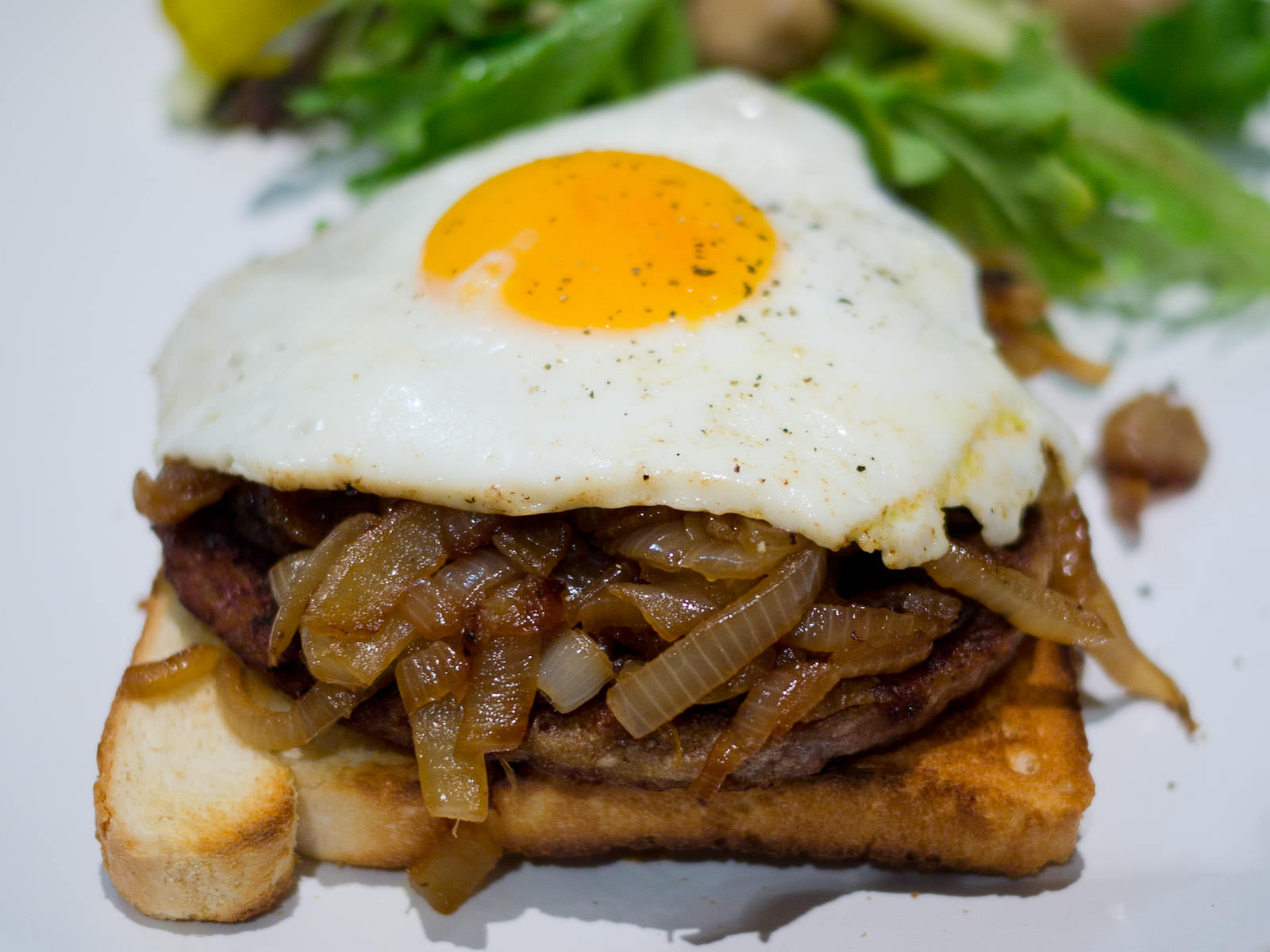 Fried egg, onions and burger pattie on toast with pickles and green salad