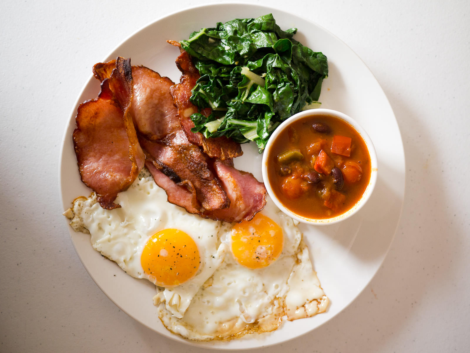 Fried eggs, bacon, garlic silverbeet, and spicy tomato, capsicum and beans